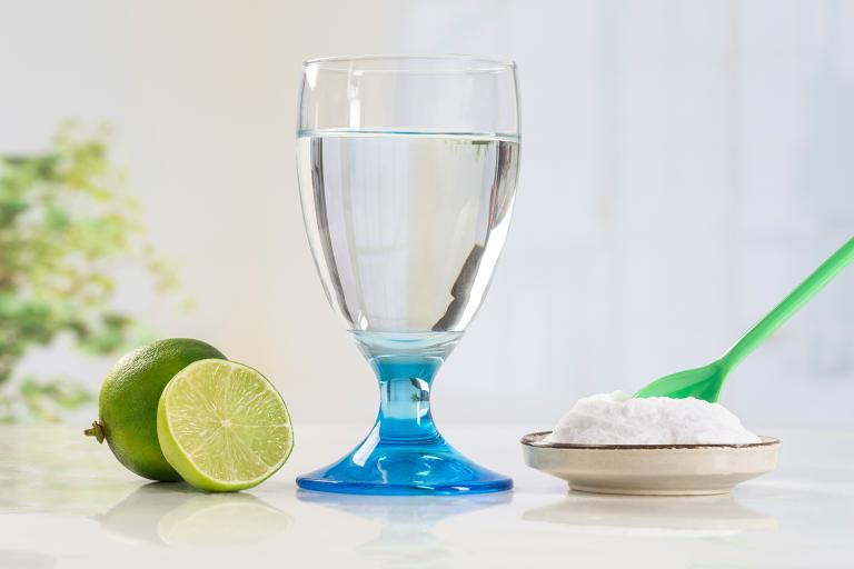 A glass of water, a sliced lime and a small dish of baking soda with a green spoon in it.